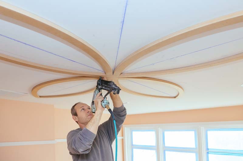 Carpenter using nail gun decorative unfinished molding on the ceiling