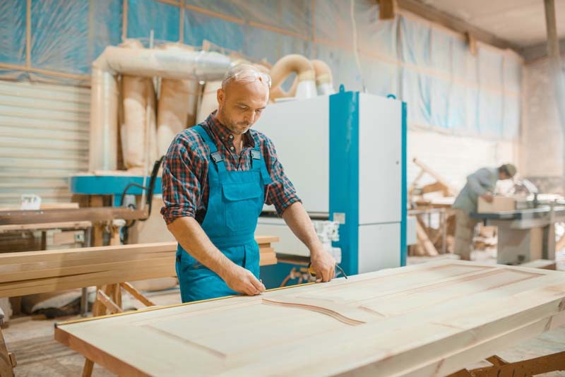 Carpenter processes wooden door, woodworking, lumber industry, carpentry. Wood processing on furniture factory, production of products of natural materials